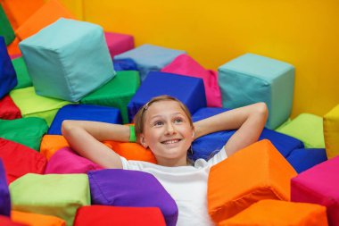 Gülümseyen ergen kız, oyun merkezinde ya da spor salonunda elleri başının arkasında canlı bir köpük küpünün içinde uzanır..