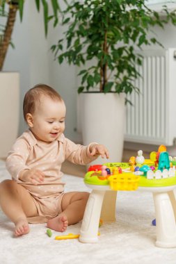 Gülümseyen bebek halının üzerinde oturur, parlak, eğitici oyuncaklarla meşgul olur, duyusal öğrenmeyi teşvik eder ve rahat ortamdaki güzel motor becerileri teşvik eder..