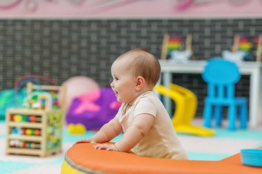 Mutlu bebek renkli mobilyaları olan parlak, oyuncak dolu bir kreşte yumuşak bir köpük yapıya tutunurken.