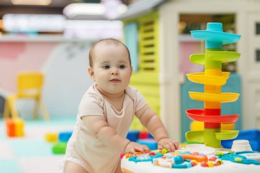 Kreşteki renkli etkileşimli oyuncak istasyonuyla ilgilenen meraklı bebek, oyun yoluyla iyi motor becerileri ve bilişsel gelişimi teşvik ediyor..