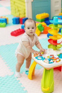 Bebek, parlak ve oyuncak dolu bir yuvada yumuşak bir paspasın üzerinde dururken renkli etkileşimli bir aktivite masasını keşfediyor..