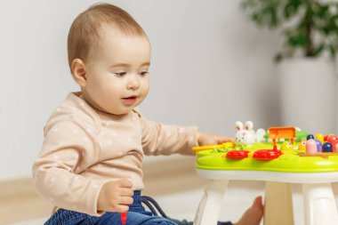 Meraklı bebek, evde yerde oturup duyusal oyun oynayarak öğrenirken, parlak ve etkileşimli bir oyuncak masasını keşfediyor..