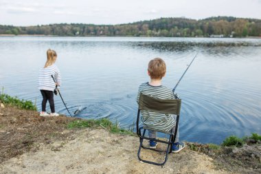 İki çocuk sessizce ormanın manzaralı gölünde balık tutuyor. Dışarıda sakin bir günün tadını çıkarıyorlar. Çubuklar ve dalgalı suyla..