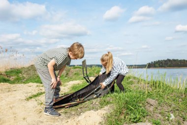 Çocuklar nehir kıyısında balık malzemeleri paketliyor.