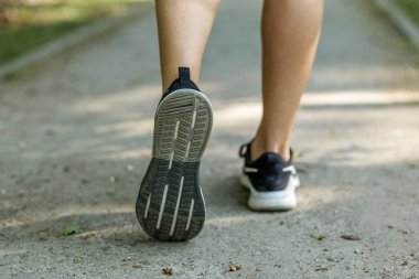 Orman yolunda yürürken atletik kadın spor ayakkabılarını detaylı bir şekilde görmek, hareket ve aktif açık hava yaşam tarzını gösteriyor.
