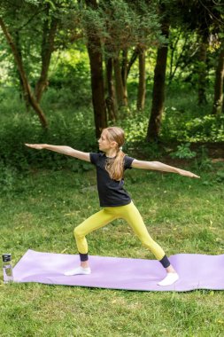 Genç bir kız yeşil bir orman parkında yoga pozu veriyor. Farkındalığı, zindeliği ve sağlıklı yaşam tarzını teşvik ediyor..