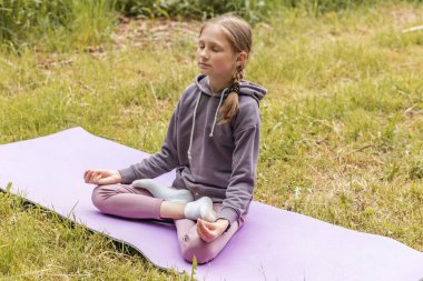 Huzurlu genç kız, Lotus pozisyonunda meditasyon yapıyor. Yoga minderi üzerinde, gözleri kapalı ve nefes almaya odaklanmış..