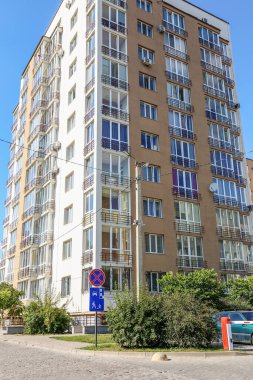 Balkonları ve geniş pencereleri olan, mavi gökyüzü ve çevresi yeşil olan kentsel alanda uzun çağdaş apartman kompleksi..