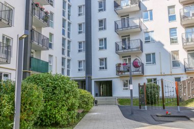 Beyaz cepheli binaların balkonları, yeşillikleri ve ortak avluda küçük çocuk parkı olan şehir yerleşkesi.