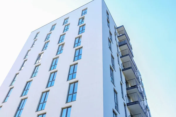Temiz beyaz duvarları, yerden tavana pencereleri ve açık mavi gökyüzünün altında siyah metal balkonları olan modern yüksek binalar..