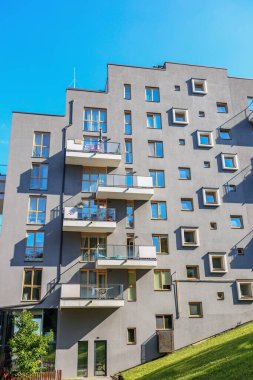 Düzensiz pencere düzenine, balkonlara ve eğimli şehir ortamında ahşap çerçeveli cam elementlere sahip gri bir apartman dairesi..