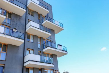 Temiz gri cepheli, ahşap çerçeveli pencereli ve saydam cam parmaklıklı birden fazla balkonlu çağdaş apartman binası.