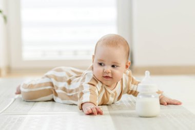 Çizgili pijamalı bebek mide zamanı süt şişesine uzanıyor. Bebek bakımı