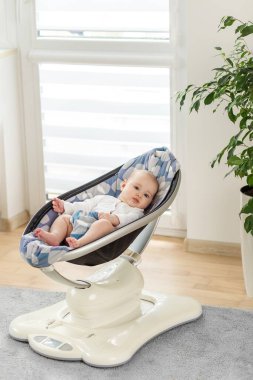 İçeride yüksek teknolojili bebek rockçı koltuğunda dinlenen beyaz tulumlu sakin bir bebek. Barışçıl, modern ebeveynlik ve bebek eşyaları konsepti.