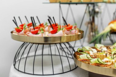 Kirazlı domatesli jambon ruloları ve altın bir büfe tepsisi üzerine yerleştirilmiş şiş yeşillikler. Etkinlikler için zarif parmak yiyecekleri.