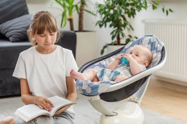 Evde sallanan bebeğin yanında otururken kitap okuyan genç bir kız, aile hayatı ve kardeşlik bağı anı..