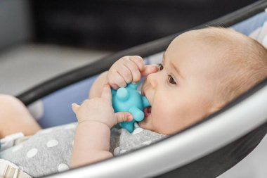 Bebeğin sallanan sandalyede yatıp silikon diş çıkarma oyuncağı, huzurlu ev ortamı ve erken çocukluk gelişimi konseptini çiğnemesi..