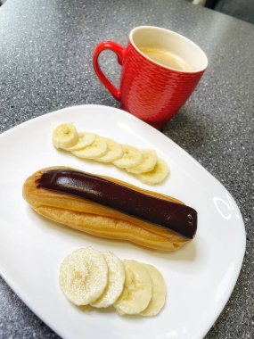 Kırmızı bardakta aromatik kahve, beyaz tabakta çikolata ve dilimlenmiş muz, tatlı, sabah