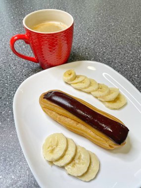 Kırmızı bardakta aromatik kahve, beyaz tabakta çikolata ve dilimlenmiş muz, tatlı, sabah