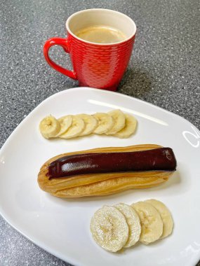 Kırmızı bardakta aromatik kahve, beyaz tabakta çikolata ve dilimlenmiş muz, tatlı, sabah