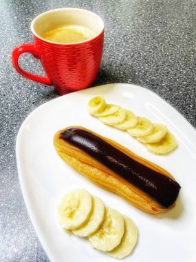 Kırmızı bardakta aromatik kahve, beyaz tabakta çikolata ve dilimlenmiş muz, tatlı, sabah