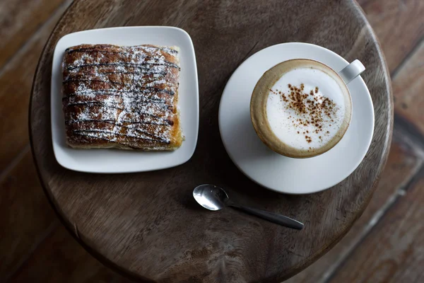 Cappuccino de aroma com croissant de chocolate na mesa de madeira vintage redonda — Fotografia de Stock