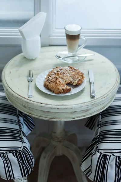 Croissant de amêndoa delicioso na mesa branca vintage com café quente latte — Fotografia de Stock