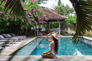 Hasır şapka havuzuyla yakınındaki rahatlatıcı kot şortlu genç ince kadın