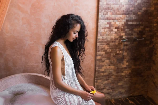 Wanita muda dalam lingerie putih santai dekat batu mandi penuh busa di kamar mandi mewah yang indah — Stok Foto
