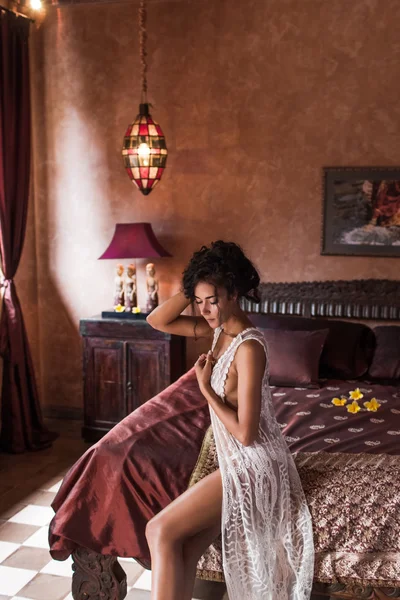 Femme aux longs cheveux noirs en lingerie de soie blanche assise sur le lit dans un hôtel de luxe le matin — Photo