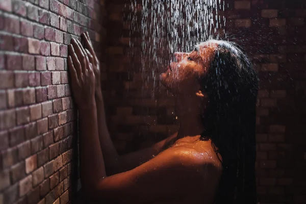 Mulher relaxante sob chuveiro quente no quarto escuro — Fotografia de Stock