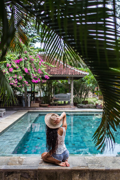 Young slim woman in jeans shorts relaxing near pool with straw hat