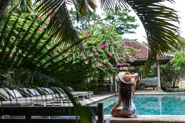 Giovane donna magra in pantaloncini jeans rilassante vicino piscina con cappello di paglia — Foto Stock