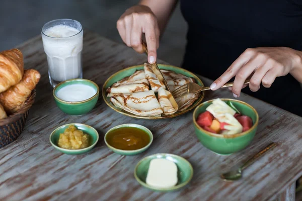 Mujer joven desayunando y cortando panqueques con tenedor de oro y cuchillo —  Fotos de Stock