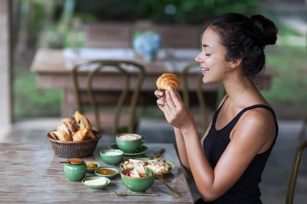 Jovem mulher desfrutando de café da manhã e segurando croissant na mão. Bom humor da manhã — Fotografia de Stock