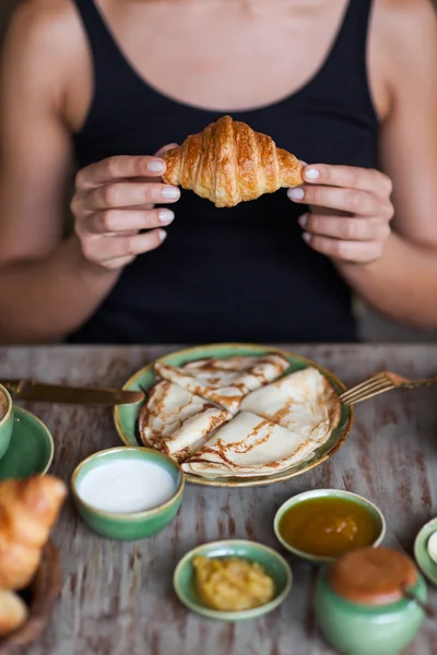 Jovem mulher desfrutando de café da manhã e segurando croissant na mão. Bom humor da manhã — Fotografia de Stock