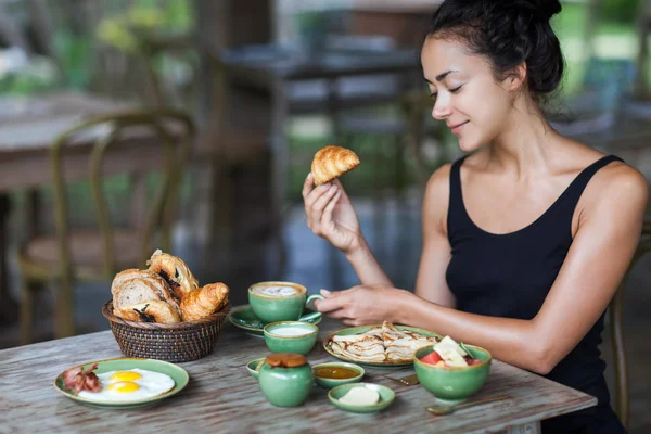 Mujer joven disfrutando del desayuno y sosteniendo croissant en la mano. Buen humor matutino —  Fotos de Stock