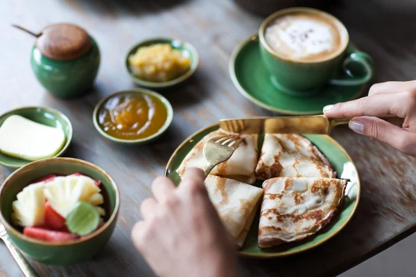 Junge Frau frühstückt und schneidet Pfannkuchen mit goldener Gabel und Messer — Stockfoto