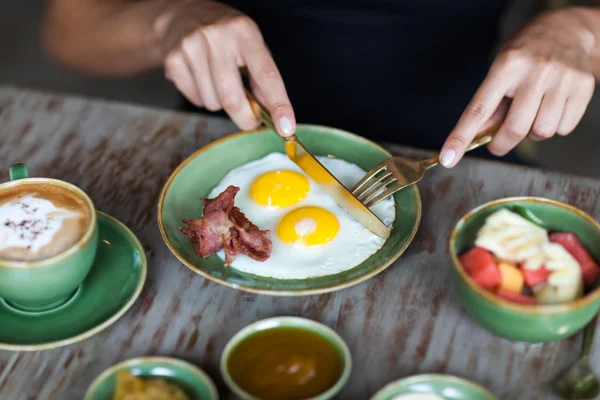 Femme coupant des œufs frits avec fourchette dorée et couteau au petit déjeuner — Photo