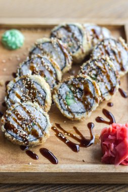Pişmiş suşi ve zencefil ve wasabi sosu ile tepesinde bir ahşap plaka rulo