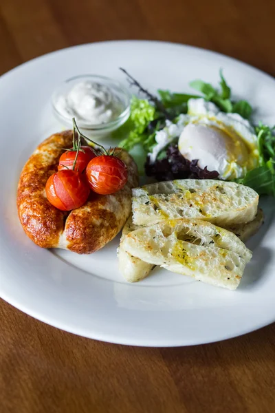 Desayuno con salchichas fritas, tomates cherry al horno, huevo escalfado y verduras —  Fotos de Stock