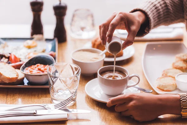 Girl pouring milk in coffee at breakfast — Stock Photo, Image