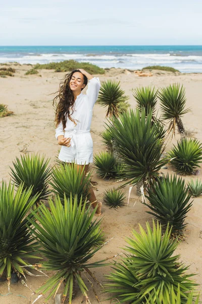 快乐的女人穿着白衬衫和短裤在沙滩上微笑 热带绿色仙人掌植物 多风的天气 — 图库照片