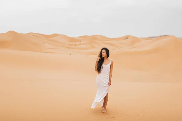 モロッコのサハラ砂漠の砂丘を歩く穏やかなシルクのドレスの美しい女性 長い髪のブルネット 東部の外観 — ストック写真