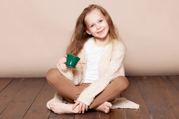 Una ragazza siede sul pavimento di legno con una tazza verde — Foto Stock