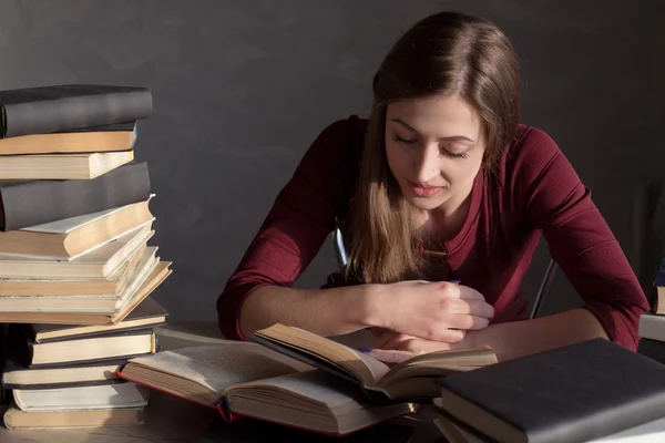 La chica sentada detrás de los libros y lee — Foto de Stock