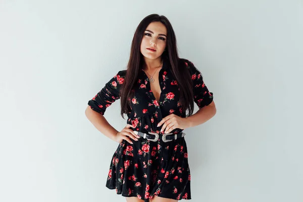 Mooie modieuze brunette vrouw in een jurk met bloemen op een witte achtergrond — Stockfoto