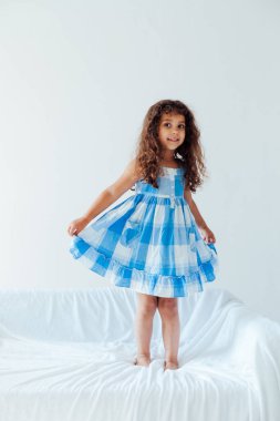 Beyaz bir kanepede mavi elbiseli güzel, kıvırcık bir kızın portresi.