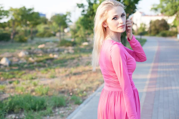 핑크 드레스를 입은 아름다운 금발의 여성이 해질 녘 공원을 산책 한다 — 스톡 사진