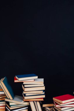 Üniversite kütüphanesinde siyah bir arkaplan üzerine okumak ve eğitim için kitap yığınları